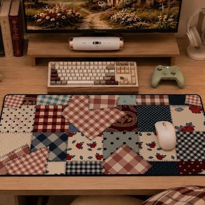 May include: A patchwork design mousepad with a variety of patterns in red, blue, and cream colors. A white mouse sits on the pad. The desk also features a keyboard, monitor, and a green game controller.