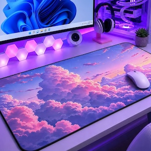 May include: A computer setup with a large monitor displaying a blue abstract design. A white computer mouse sits on a long mousepad with a cloudscape design. The setup includes a white computer tower with internal lighting and a pair of headphones.