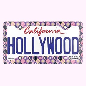 Może przedstawiać: Dekoracyjna tablica rejestracyjna z napisem "HOLLYWOOD" w kolorze niebieskim. Słowo "California" jest napisane czerwoną czcionką u g&oacute;ry. Obramowanie ma powtarzający się wz&oacute;r gwiazd, księżyc&oacute;w i romb&oacute;w w kolorze r&oacute;żowym, fioletowym i białym.