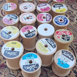 May include: A collection of vintage wooden sewing thread spools featuring various brands including Talon, Lily, and Star. Each spool has a circular paper label on top displaying brand names, colour numbers, yardage, and prices in cents.
