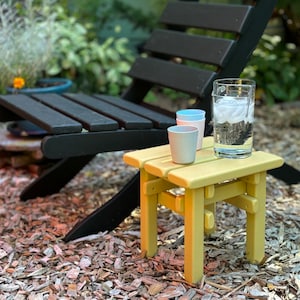 May include: A yellow wooden side table with a glass of ice water and two small cups on top. The table is sitting on a bed of wood chips.