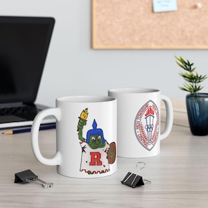 Può includere: Due tazze in ceramica bianca. Una tazza presenta un personaggio a forma di rana dei cartoni animati che tiene una torcia e uno scudo, indossa un elmo e una maglietta con una grande "R". L'altra tazza mostra un emblema scolastico con la scritta "Rich Township High School Central Campus".