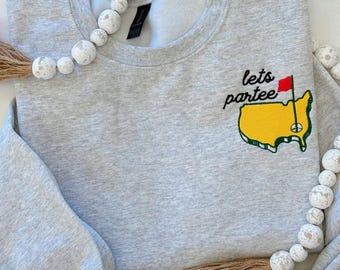 May include: Gray sweatshirt with a yellow and green embroidered patch that says "lets partee" with a red flag on a golf course.
