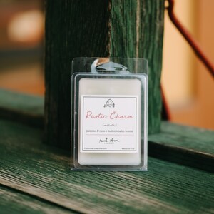 May include: A white wax melt in a clear plastic container with a label that reads "Rustic Charm (mello lake) Jasmine & rose melon calm woods Rustic Charm Candies rusticcharmcandies.com wax melt 2 oz."