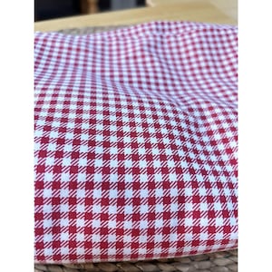 Puede incluir: Primer plano de una tela a cuadros rojos y blancos. El patrón es un diseño clásico de cuadros, con cuadrados pequeños y espaciados uniformemente. La tela parece ser de algodón o un material similar, y está doblada.