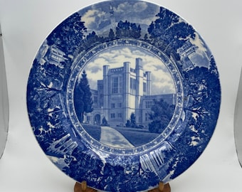 May include: Blue and white ceramic plate with a blue and white image of a building in the center. The building is surrounded by trees and a path. The plate has a blue and white border.