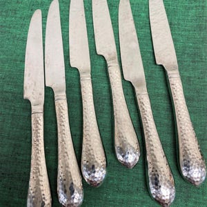 May include: Set of six silver-toned dinner knives with hammered handles. The knives have a classic design and are perfect for everyday use.