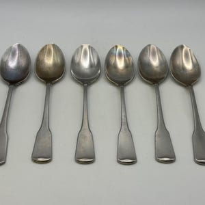 May include: Six silver spoons with a polished finish. The spoons are arranged in a row, with the bowls facing the viewer.