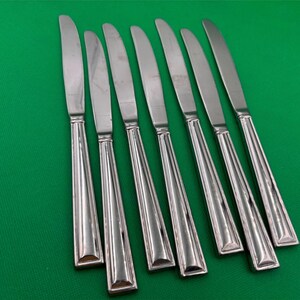 May include: A set of seven silver dinner knives with a decorative pattern on the handles.