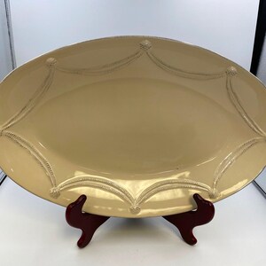 May include: A large, oval-shaped serving platter with a cream-colored glaze and decorative raised edges. The platter is on a red stand.