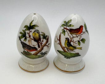 May include: Two white ceramic salt and pepper shakers shaped like eggs with a gold trim. Each shaker features a different bird design with green leaves and branches.