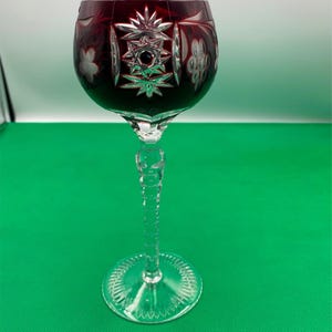 May include: A tall, clear wine glass with a deep red, cut-glass bowl. The bowl is decorated with a white, geometric pattern. The stem is long and slender.