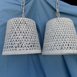 May include: Two white, cone-shaped pendant lights with a geometric triangle pattern. The lamps are suspended from white chains against a blue background. The lampshades have a woven appearance.