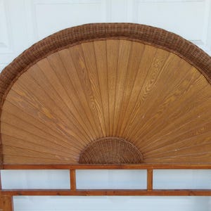 May include: A wooden headboard with a fan-shaped design. The center is made of light brown wood, with a woven wicker border and a small woven wicker semi-circle at the bottom. The headboard is supported by a wooden frame.