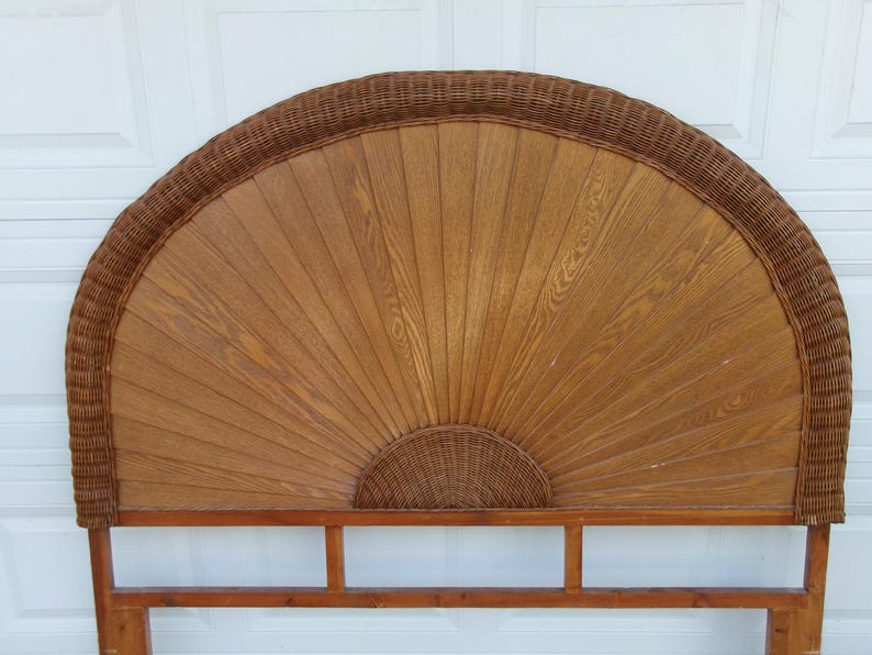 May include: A wooden headboard with a fan-shaped design. The center is made of light brown wood, with a woven wicker border and a small woven wicker semi-circle at the bottom. The headboard is supported by a wooden frame.