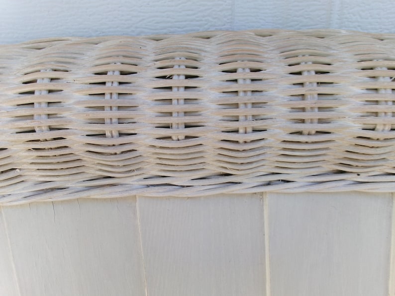 May include: Close-up of a section of a white wicker chair. The image shows the woven texture of the wicker, with horizontal and vertical lines creating a grid pattern. The chair's frame is visible at the bottom, painted in a matching white.