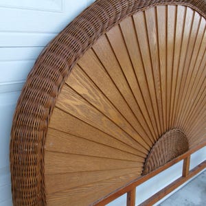 May include: A brown wicker and wood headboard. The headboard features a fan-shaped design with wooden slats and a woven wicker border. The headboard is supported by a wooden frame. The headboard is a decorative element for a bed.