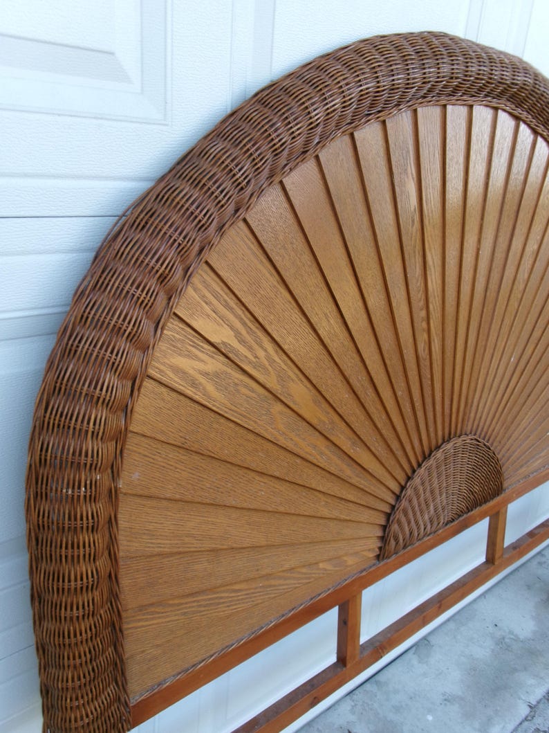 May include: A brown wicker and wood headboard. The headboard features a fan-shaped design with wooden slats and a woven wicker border. The headboard is supported by a wooden frame. The headboard is a decorative element for a bed.