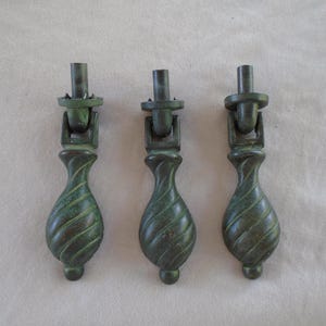 May include: Three antique bronze drawer pulls with a twisted, teardrop-shaped design. Each pull features a dark green patina and a decorative top with a mounting post. These vintage hardware pieces are ideal for furniture restoration projects.