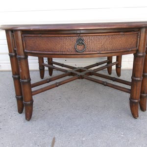 May include: A round, dark brown coffee table with a woven drawer and bamboo-style legs. The table has a dark metal ring pull on the drawer and measures approximately 36 inches in diameter.