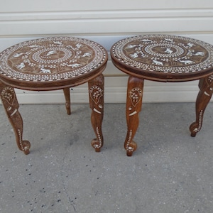Puede incluir: Dos mesas auxiliares redondas de madera con intrincados diseños incrustados. Las mesas de color marrón oscuro presentan patrones blancos de animales y flores en la mesa y las patas. Las mesas tienen patas curvas y miden unos 46 cm de diámetro.