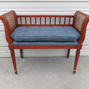 May include: A vintage bench with a reddish-brown wooden frame, featuring woven cane side panels and a blue cushion with a white dot pattern. The bench has a slatted back and turned legs, offering a classic aesthetic.
