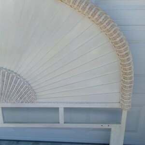 May include: Off-white wicker headboard with a fan-shaped design. The headboard features a woven wicker border and a solid wood frame. The headboard is supported by a wooden base.