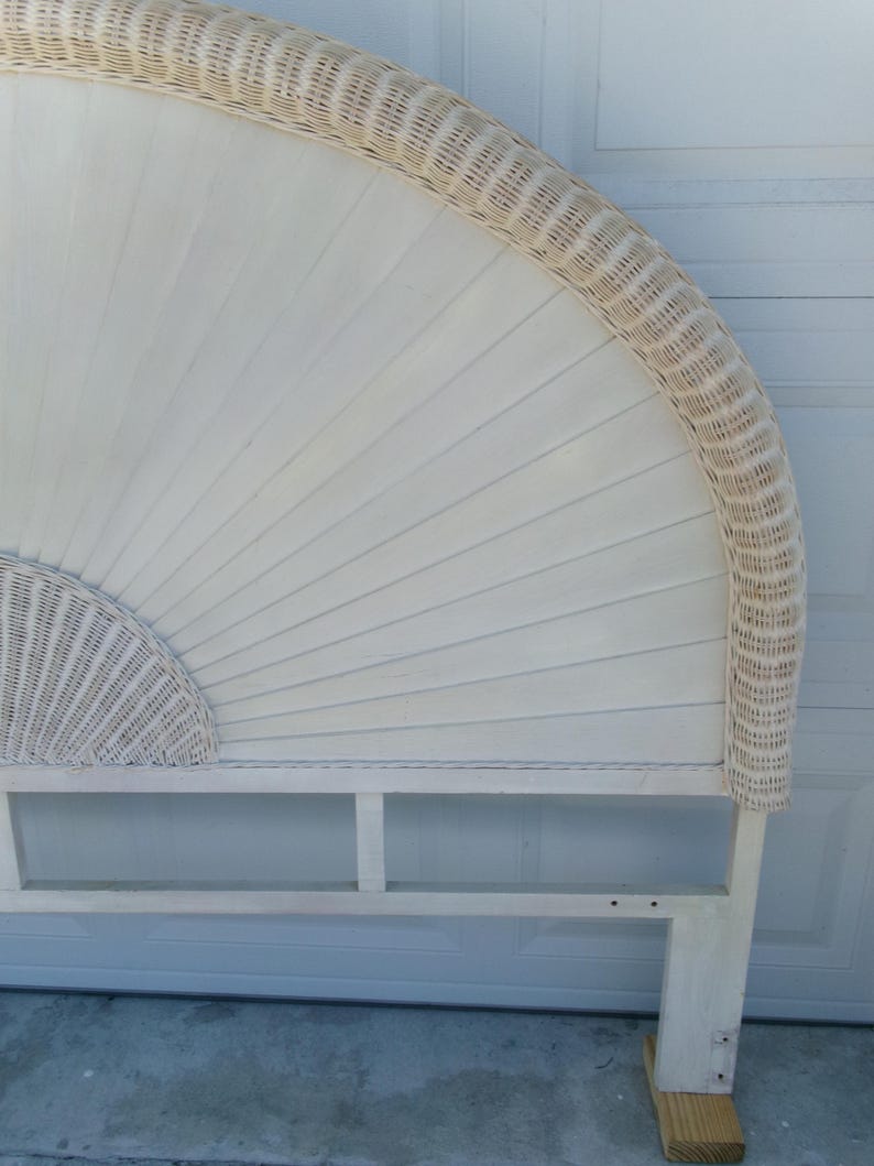 May include: Off-white wicker headboard with a fan-shaped design. The headboard features a woven wicker border and a solid wood frame. The headboard is supported by a wooden base.