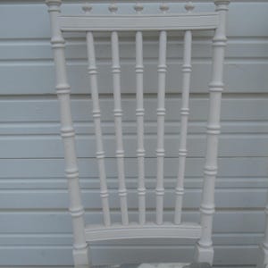 May include: A white painted chair with a bamboo-style back and vertical slats. The chair has a decorative top with small crown-like details. The seat has a patterned fabric with shades of blue, gray, and beige.