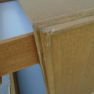 Puede incluir: Primer plano de un escritorio de madera marr&oacute;n claro con un caj&oacute;n parcialmente abierto. El escritorio tiene una parte superior rectangular y un borde decorativo. El interior del caj&oacute;n es blanco. La veta de la madera es visible y hay peque&ntilde;os signos de desgaste.