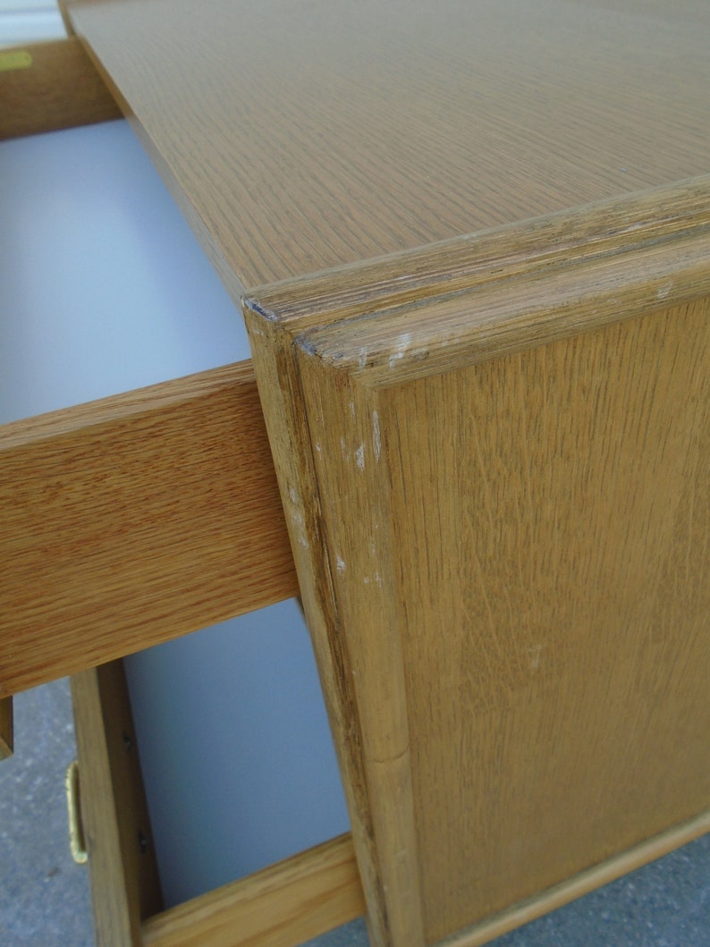 Puede incluir: Primer plano de un escritorio de madera marr&oacute;n claro con un caj&oacute;n parcialmente abierto. El escritorio tiene una parte superior rectangular y un borde decorativo. El interior del caj&oacute;n es blanco. La veta de la madera es visible y hay peque&ntilde;os signos de desgaste.
