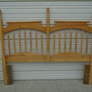 May include: A wooden headboard with a spindle design. The headboard is made of light wood and has a simple, classic style.
