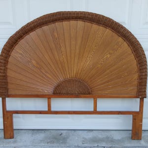 May include: A vintage headboard with a fan-shaped design. The headboard features a wooden frame with a woven rattan border and a central panel of vertical wooden slats. The color is a warm brown, with a natural wood grain visible.