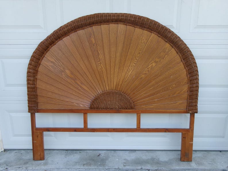 May include: A vintage headboard with a fan-shaped design. The headboard features a wooden frame with a woven rattan border and a central panel of vertical wooden slats. The color is a warm brown, with a natural wood grain visible.