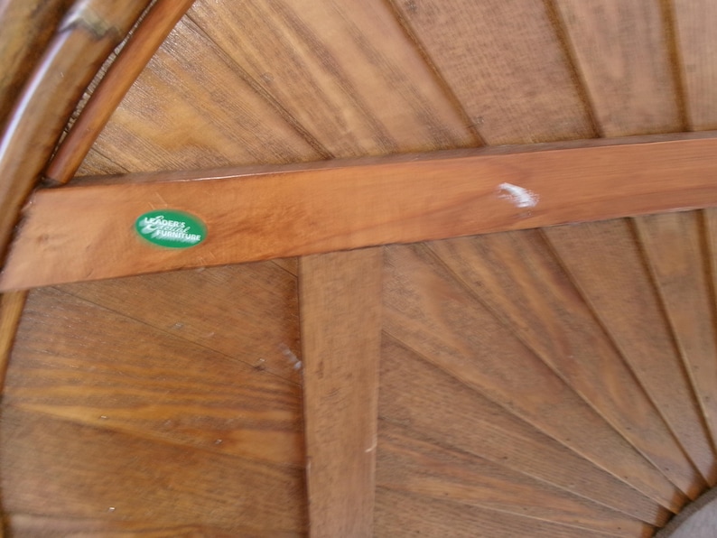 May include: Close-up of a wooden gazebo roof with a fan-like design. The wood has a warm, natural tone with visible grain. A green oval sticker with white text is affixed to a horizontal beam. The gazebo's structure is made of wood.