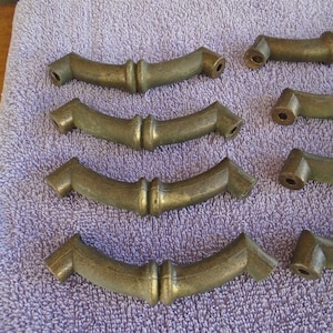 May include: Set of eight antique brass cabinet pulls with a bamboo design. The pulls are in the shape of a curved arch with a decorative knob in the center.