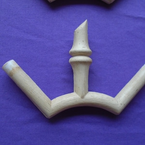 May include: A light-colored wooden decorative object with a central vertical element and two angled arms. The object has a natural wood grain and is set against a purple background. The top of the central element is cut at an angle.