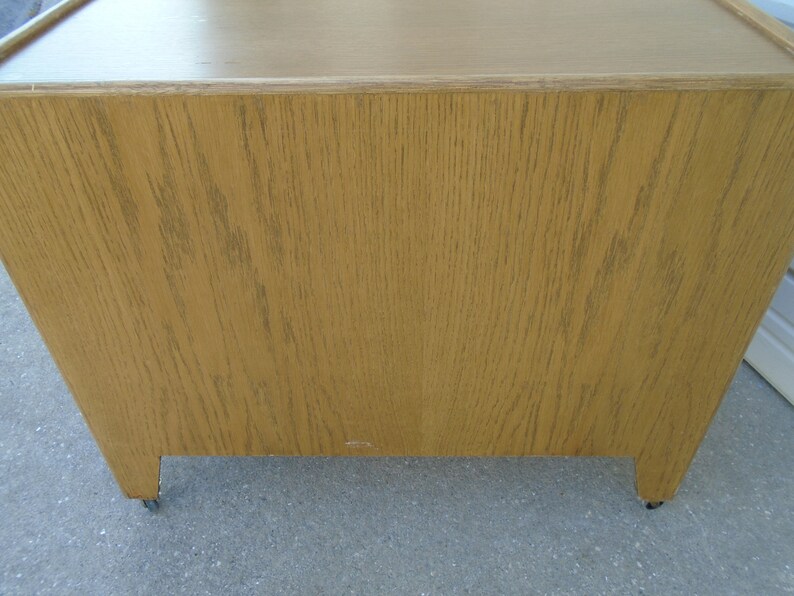 Puede incluir: Un mueble de madera marr&oacute;n claro con forma rectangular. El mueble tiene un patr&oacute;n de vetas de madera natural y se apoya sobre peque&ntilde;as ruedas. El dise&ntilde;o del mueble es sencillo y funcional.