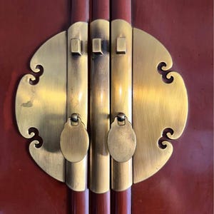 May include: Close-up of a brass latch with ornate details on a red wooden cabinet door.