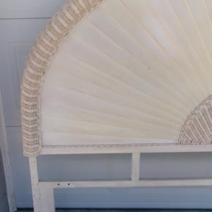 May include: Off-white wicker headboard with a fan-shaped design. The headboard features a woven wicker border and a panel of vertical wooden slats. The frame is made of light-colored wood, creating a neutral and natural aesthetic.