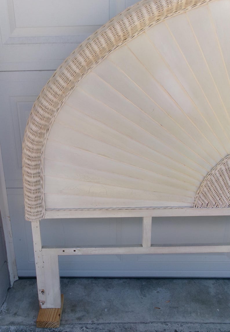 May include: Off-white wicker headboard with a fan-shaped design. The headboard features a woven wicker border and a panel of vertical wooden slats. The frame is made of light-colored wood, creating a neutral and natural aesthetic.