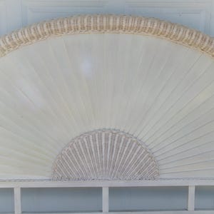 May include: Off-white wicker headboard with a fan-shaped design. The headboard features a woven wicker border and a semi-circular woven wicker accent at the bottom. The main body is made of vertical wooden slats.