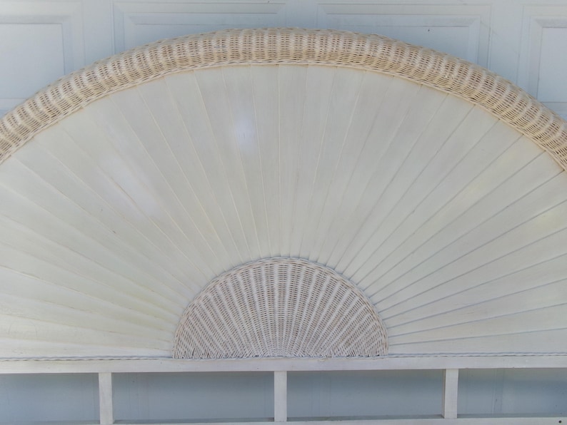 May include: Off-white wicker headboard with a fan-shaped design. The headboard features a woven wicker border and a semi-circular woven wicker accent at the bottom. The main body is made of vertical wooden slats.