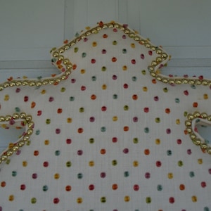 May include: A white headboard with a gold trim and a colorful polka dot pattern.