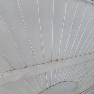 May include: A close-up view of a white wooden ceiling with a curved design. The ceiling is constructed of narrow, parallel planks, creating a textured surface. The planks are painted in a light, neutral white color.