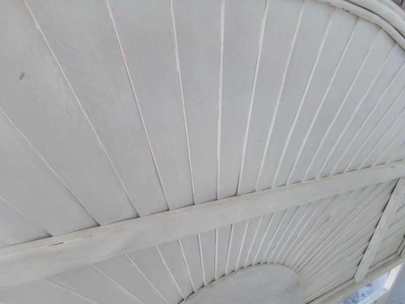 May include: A close-up view of a white wooden ceiling with a curved design. The ceiling is constructed of narrow, parallel planks, creating a textured surface. The planks are painted in a light, neutral white color.