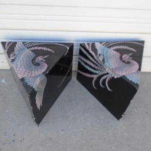 May include: Two black triangular end tables with a painted design of a pink and blue bird with a long tail. The tables are made of wood and have a glossy finish.