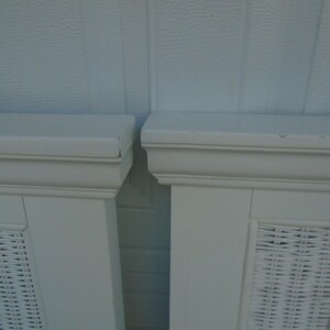 May include: Two white painted cabinet doors with woven wicker panels. The doors have a rectangular shape with a decorative top molding. The background is a light blue textured wall.