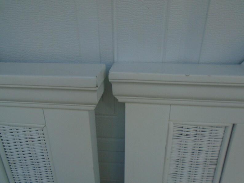 May include: Two white painted cabinet doors with woven wicker panels. The doors have a rectangular shape with a decorative top molding. The background is a light blue textured wall.
