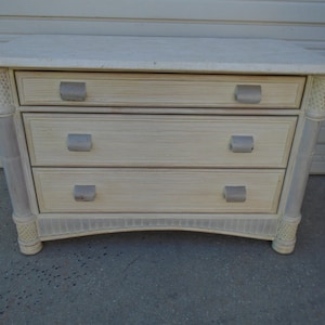May include: A white three-drawer dresser with a marble top. The dresser has a slightly curved front and decorative details on the sides.
